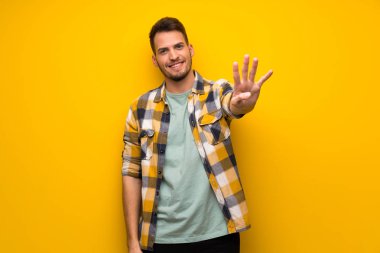 Sarı duvar mutlu ve sayım dört parmak ile yakışıklı adam