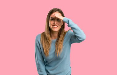 Bir şey izole pembe arka plan bakmak için sarışın kadın mavi tişört uzakta el ile seyir ile