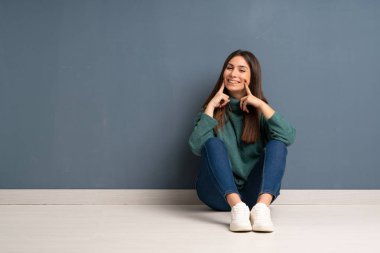 Genç bir kadın yerde oturmuş mutlu ve mutlu bir ifadeyle gülümsüyor