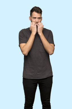Gergin ve korkmuş putting eller ağız için mavi arka plan üzerinde siyah gömlek adamla