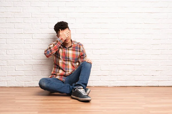 Young man sitting on the floor covering eyes by hands. Do not want to see something