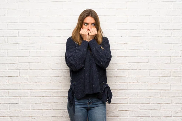 Blonde woman over brick wall nervous and scared stretching hands to the front