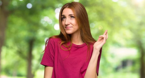 Young redhead girl with fingers crossing and wishing the best in the park