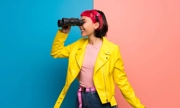 Young woman with yellow jacket and looking in the distance with binoculars