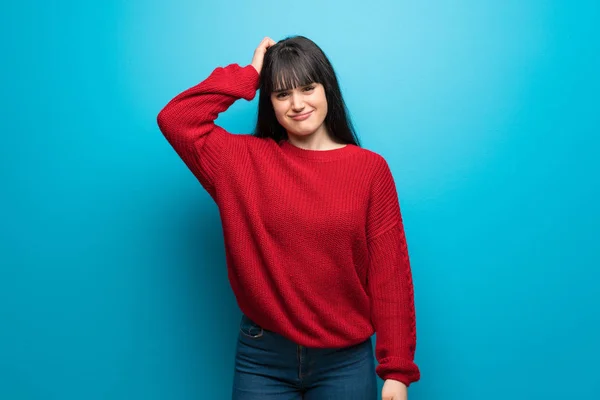 Woman with red sweater over blue wall with an expression of frustration and not understanding