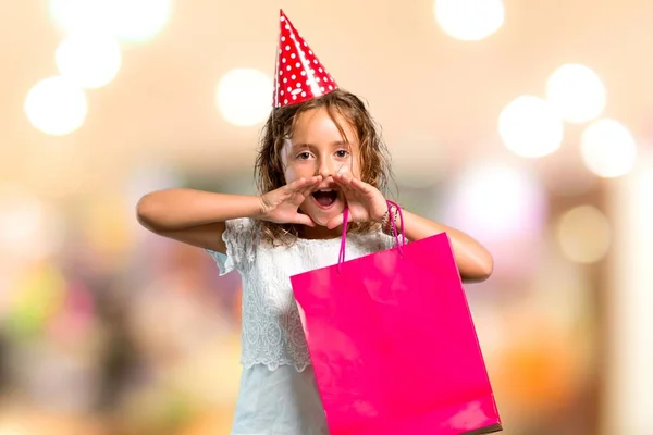 Bambina ad una festa di compleanno che tiene una borsa regalo gridando con la bocca spalancata su sfondo sfocato — Foto Stock