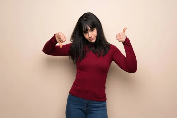 Young woman with red turtleneck making good-bad sign. Undecided between yes or not