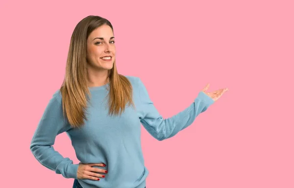 青いシャツの背面を指すと分離ピンク背景に製品を提示とブロンドの女性 — ストック写真