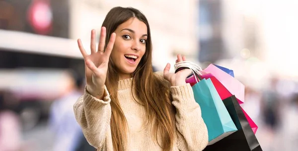 Young girl with shopping bags happy and counting four with fingers in the city