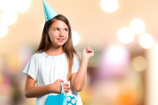 Menina em uma festa de aniversário segurando um saco de presente apontando com o dedo indicador uma ótima ideia sobre fundo desfocado — Fotografia de Stock