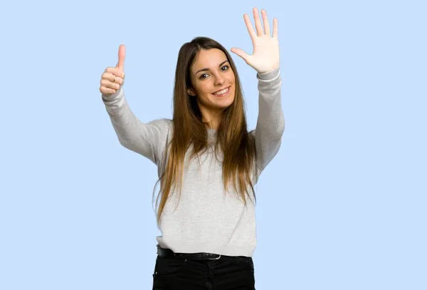 young girl counting six with fingers on blue background