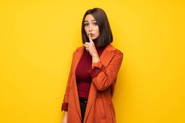 Young woman with coat showing a sign of silence gesture putting finger in mouth