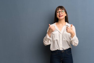 Her iki el ile jest Yaşasın vererek ve gülümseyen mavi duvarın üzerinden gözlüklü kadın