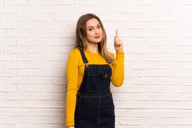 Genç kız harika bir fikir işaret parmağı ile işaret beyaz tuğla duvarın üzerinden