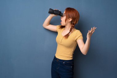 Mavi arka plan ve Uzaktan dürbünle bakarak genç Kızıl saçlı kadın