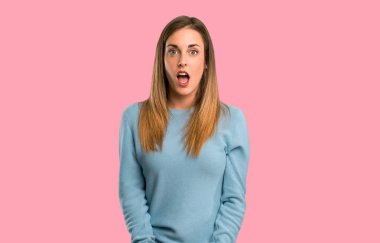 Sürpriz ve izole pembe bir arka plan üzerinde şok yüz ifadesi ile mavi gömlek ile sarışın kadın