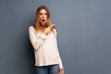 Sarışın kadın şaşırttı ve yan işaret gri arka plan üzerinde