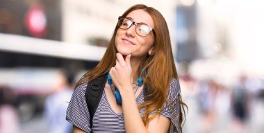 Kızıl saçlı öğrenci kadınla gözlük ve şehirde gülümseyen