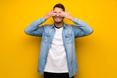 Sarı duvar eller tarafından gözleri kaplama yakışıklı adam. İleride ne olduğunu görmek için sürpriz