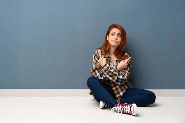 Jovem Ruiva Sentada Chão Apontando Para Laterais Com Dúvidas — Fotografia de Stock