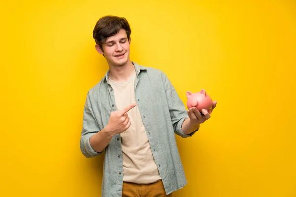 Tonåringen Man Över Gula Väggen Håller Piggybank — Stockfoto