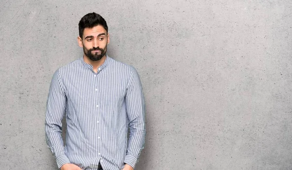 Elegant man with shirt with confuse face expression while bites lip over textured wall