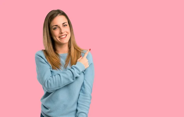 金发碧眼的女人与蓝色衬衫指向一边 提出一个产品在孤立的粉红色背景 — 图库照片