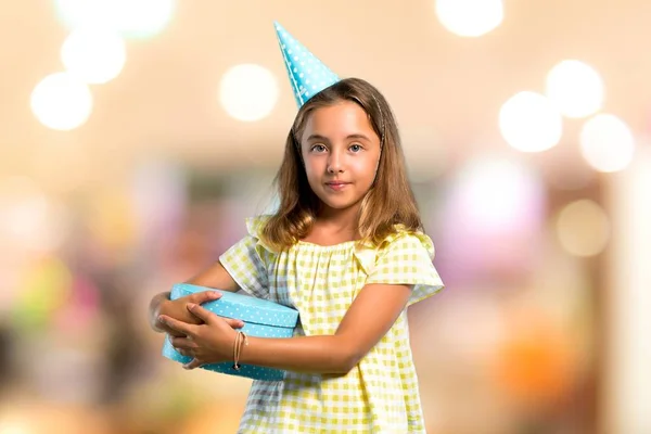 Little girl at a birthday party holding a gift keeping arms crossed on unfocused background