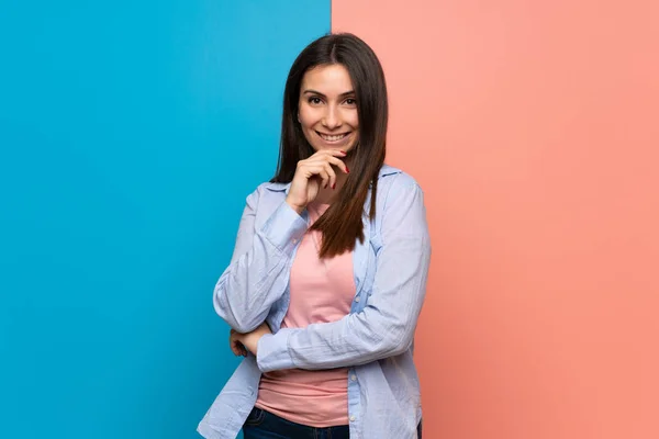 Young woman over pink and blue wall smiling and looking to the front with confident face