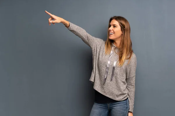 Mujer Rubia Sobre Fondo Gris Apuntando Lejos —  Fotos de Stock