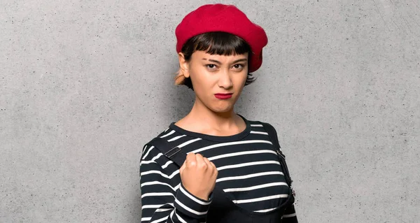Young woman with beret with angry gesture over textured wall