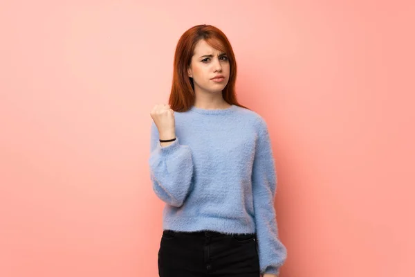 Young redhead woman over pink background with angry gesture