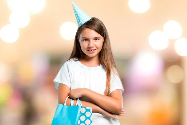 Menina em uma festa de aniversário segurando um saco de presente mantendo os braços cruzados em fundo desfocado — Fotografia de Stock