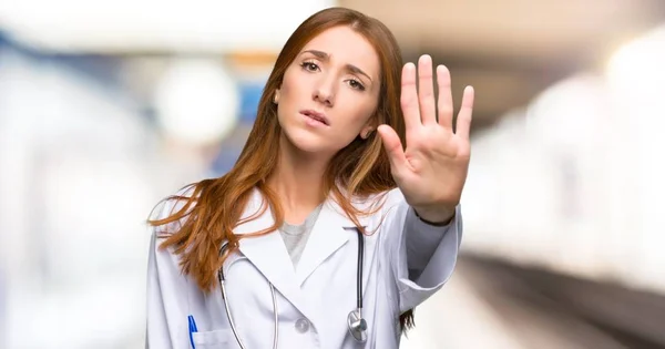 Redhead doctor woman making stop gesture denying a situation that thinks wrong in the hospital