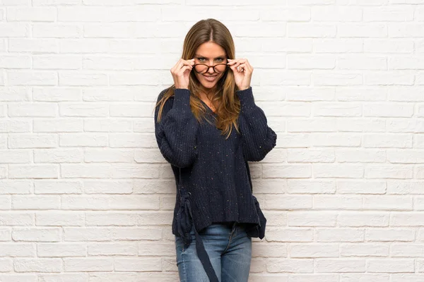 Blonde woman over brick wall with glasses and surprised