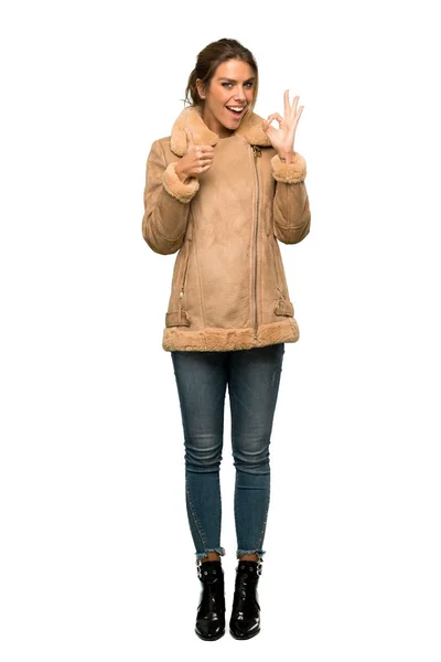 一个金发碧眼的女人的全长镜头与外套显示确定的标志 并在孤立的白色背景上竖起一个拇指的手势 — 图库照片