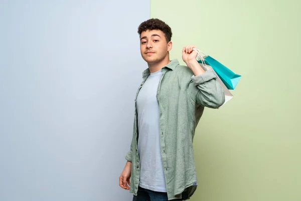 Junger Mann Über Blauem Und Grünem Hintergrund Mit Vielen Einkaufstaschen — Stockfoto