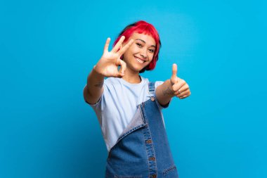 Ok işareti ve jest yukarı gösteren mavi duvarın üzerinden pembe saçlı genç kadın