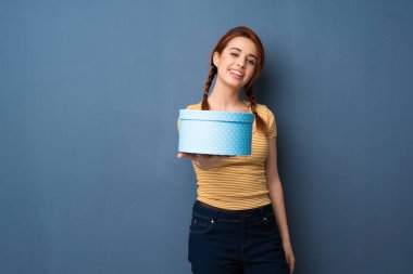 Mavi renkli bir hediye elinde tutan genç Kızıl saçlı kadın