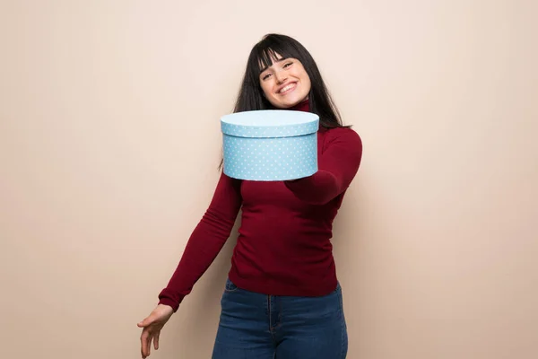 Young woman with red turtleneck holding a gift in hands