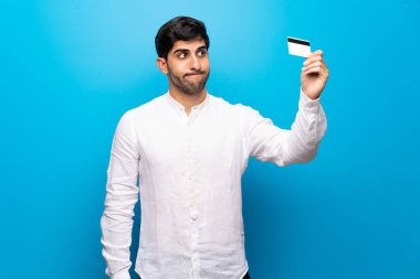 Genç adam bir kredi kartı olmadan para alarak izole mavi duvarın üzerinden