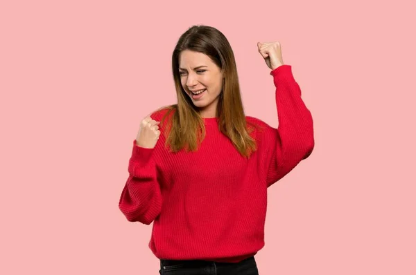 孤立したピンク色の背景上の勝利を祝う赤いセーターを持つ若い女性 — ストック写真