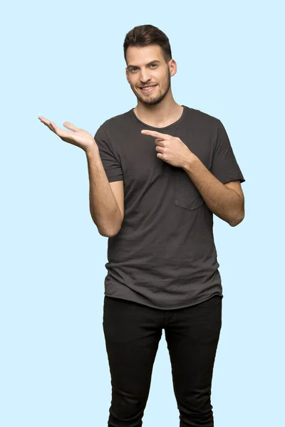手のひらに架空 Copyspace を保持している黒の シャツと青い背景に広告を挿入する男 — ストック写真