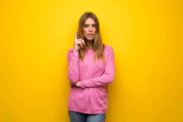 指を上向きにするアイデアを考えて黄色の壁にピンクのセーターの女性 — ストック写真