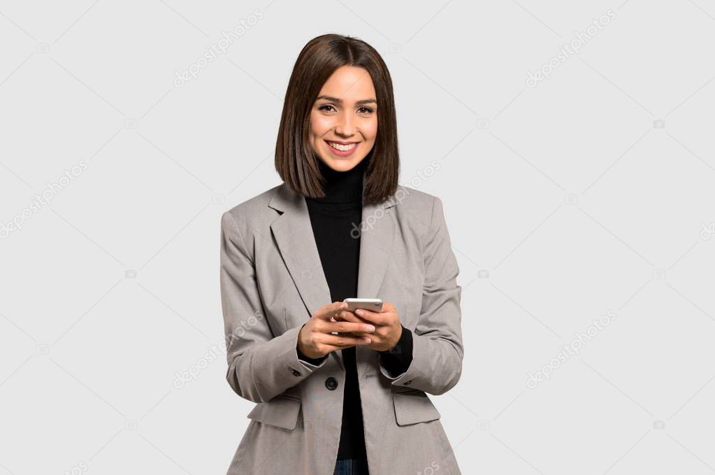 Young business woman sending a message with the mobile on isolated grey background