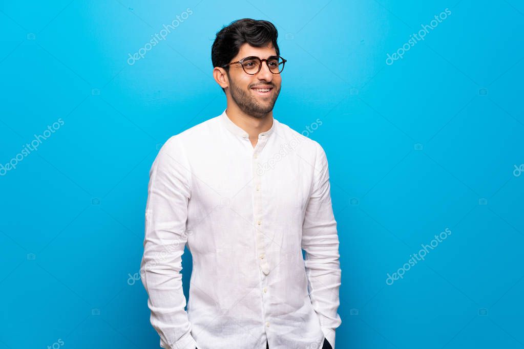 Young man over isolated blue wall with glasses and smiling