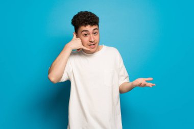 Telefon jest yapma ve şüphe mavi arka plan üzerinde genç adam