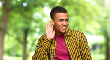 Genç afro Amerikalı adam bir şey bir parkta kulak el koyarak dinleme