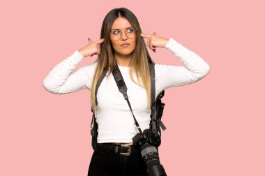 Her iki kulak izole pembe bir arka plan üzerinde elleriyle kapsayan genç fotoğrafçı kadın