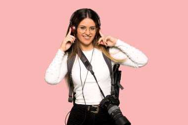 Genç fotoğrafçı kadın izole pembe bir arka plan üzerinde kulaklık ile müzik dinlemek